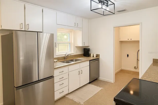 a kitchen with stainless steel appliances granite countertop a refrigerator a sink and white cabinets