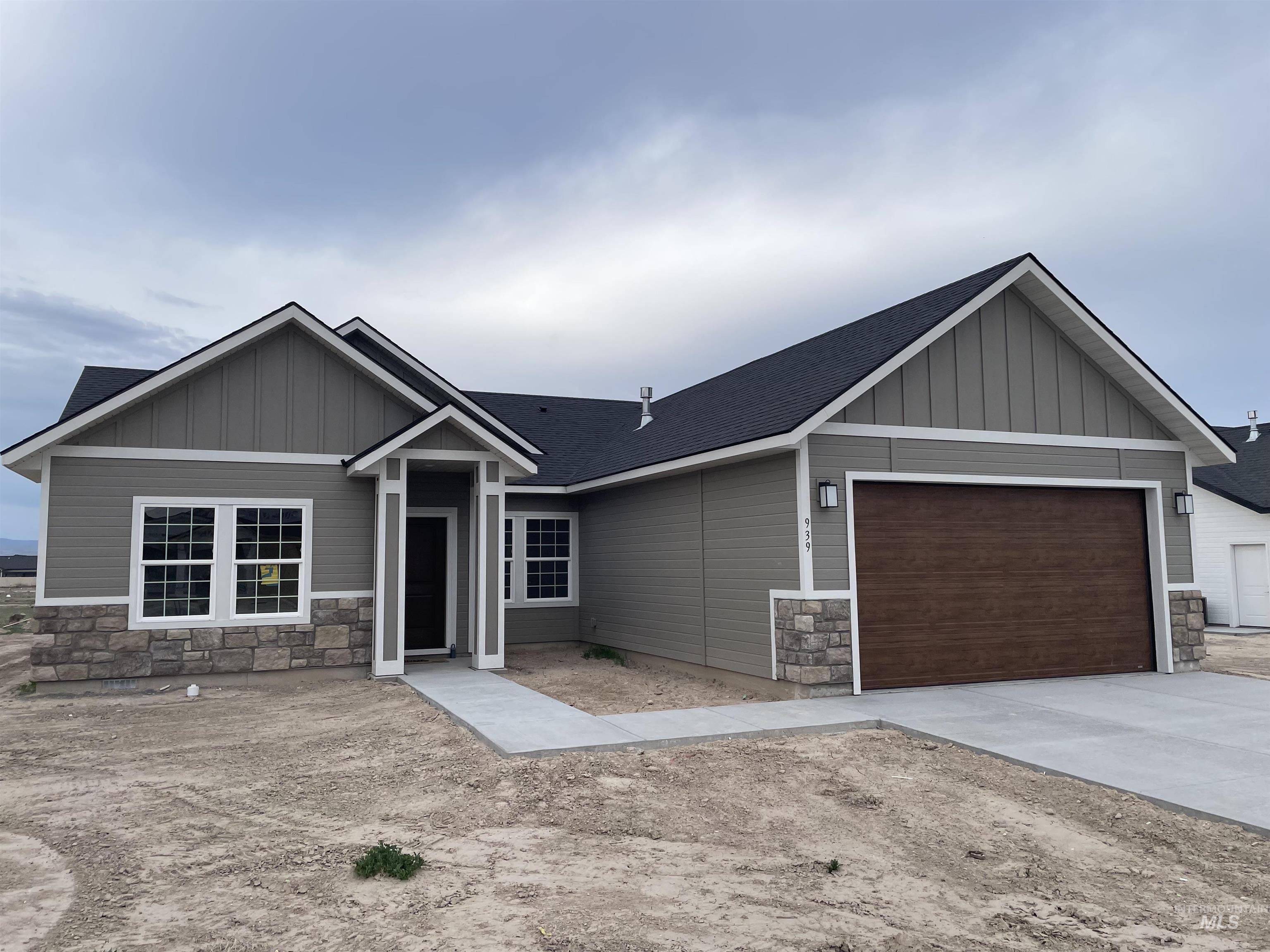 Craftsman inspired home featuring board and batten siding, stone siding, a garage, and driveway