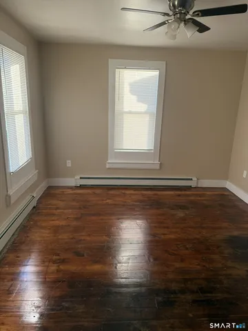 an empty room with wooden floor and windows with curtains