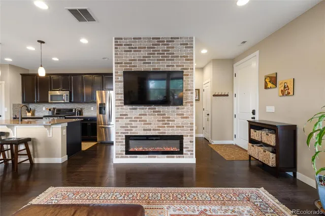a living room with stainless steel appliances furniture a fireplace a flat screen tv and kitchen view