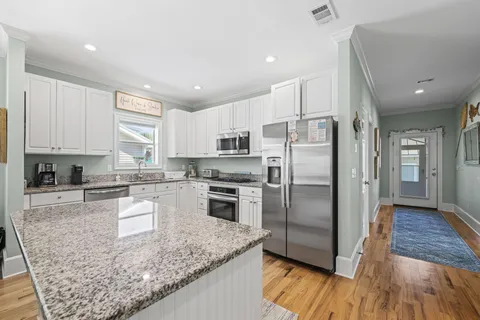 a kitchen with granite countertop a refrigerator oven a sink dishwasher and white cabinets with wooden floor