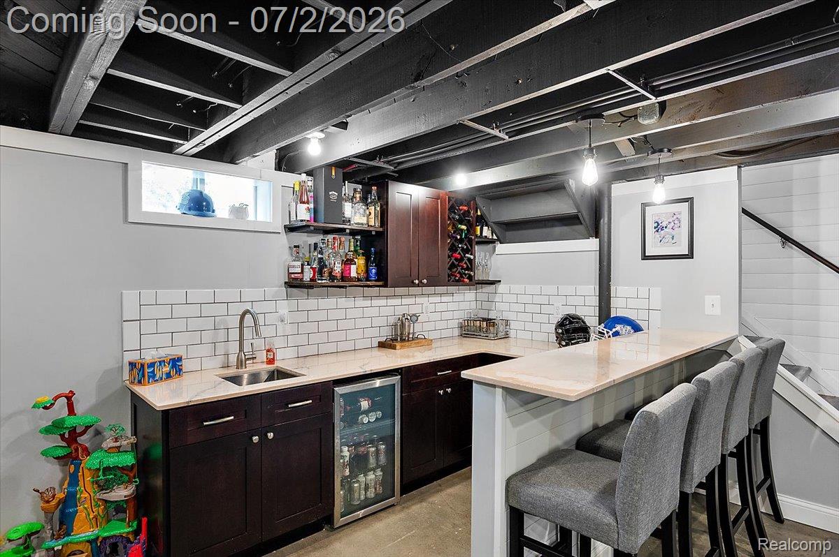 1706 Princeton Road Berkley, MI 48072 - Photo 40 of 49 Full-service wet bar featuring dark wood cabinetry, a built-in beverage refrigerator, subway tile backsplash, and a light-toned countertop with seating for three