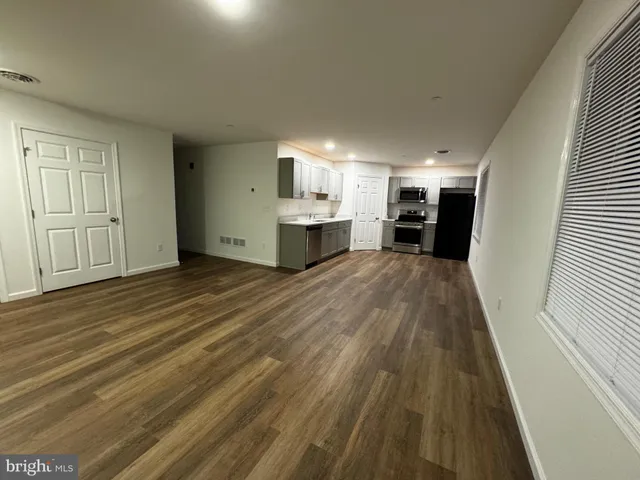 an empty room with wooden floor kitchen view and windows