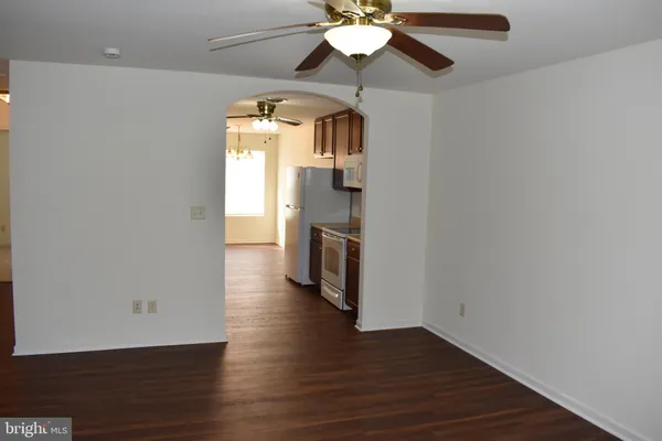 an empty room with wooden floor a ceiling fan and kitchen view