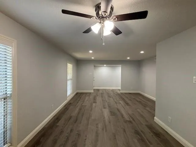 an empty room with wooden floor ceiling fan and windows
