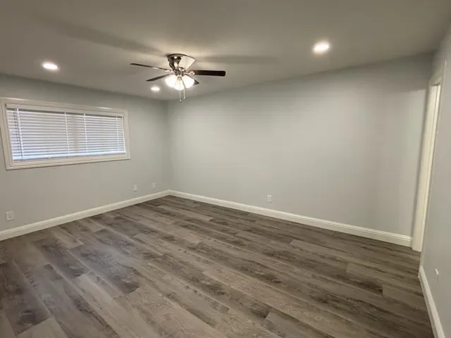 an empty room with wooden floor fan and windows