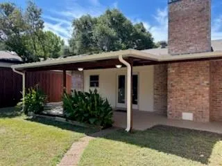 a view of a white house with a small yard plants and a large tree