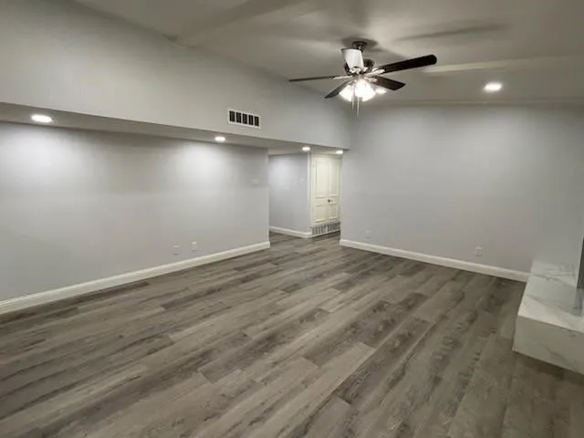 an empty room with wooden floor fan and windows