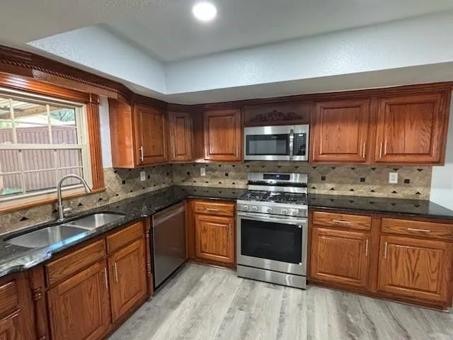 a kitchen with stainless steel appliances granite countertop wooden cabinets a stove a sink and dishwasher with wooden floor