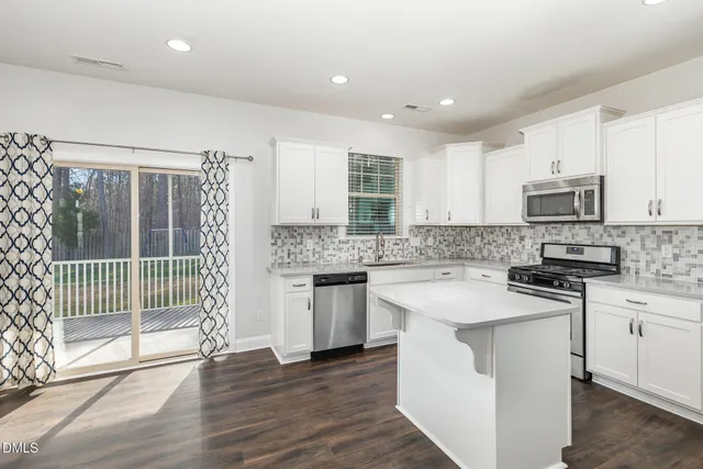 a kitchen with stainless steel appliances a refrigerator a sink dishwasher a stove top oven a refrigerator with white cabinets and wooden floor