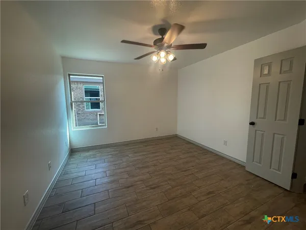 an empty room with wooden floor fan and windows