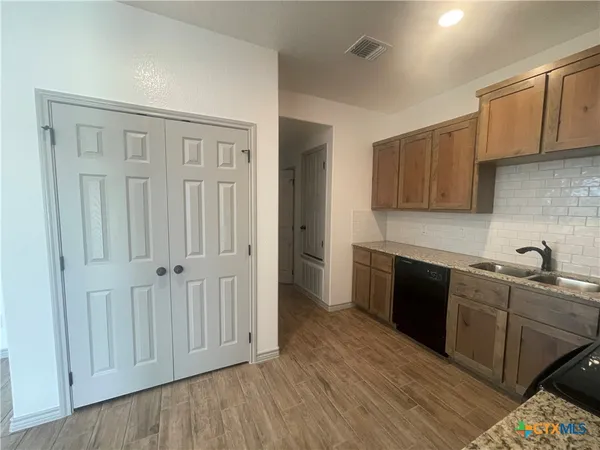 a kitchen with stainless steel appliances granite countertop a refrigerator a sink dishwasher and wooden cabinets with wooden floor