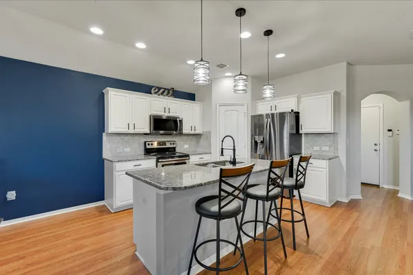 a kitchen with stainless steel appliances kitchen island granite countertop a table chairs refrigerator and microwave