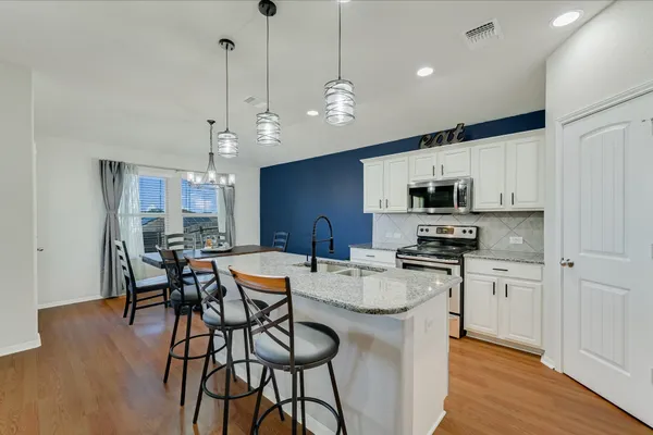 a kitchen with stainless steel appliances granite countertop a stove a refrigerator a kitchen island a sink and a refrigerator with wooden floor