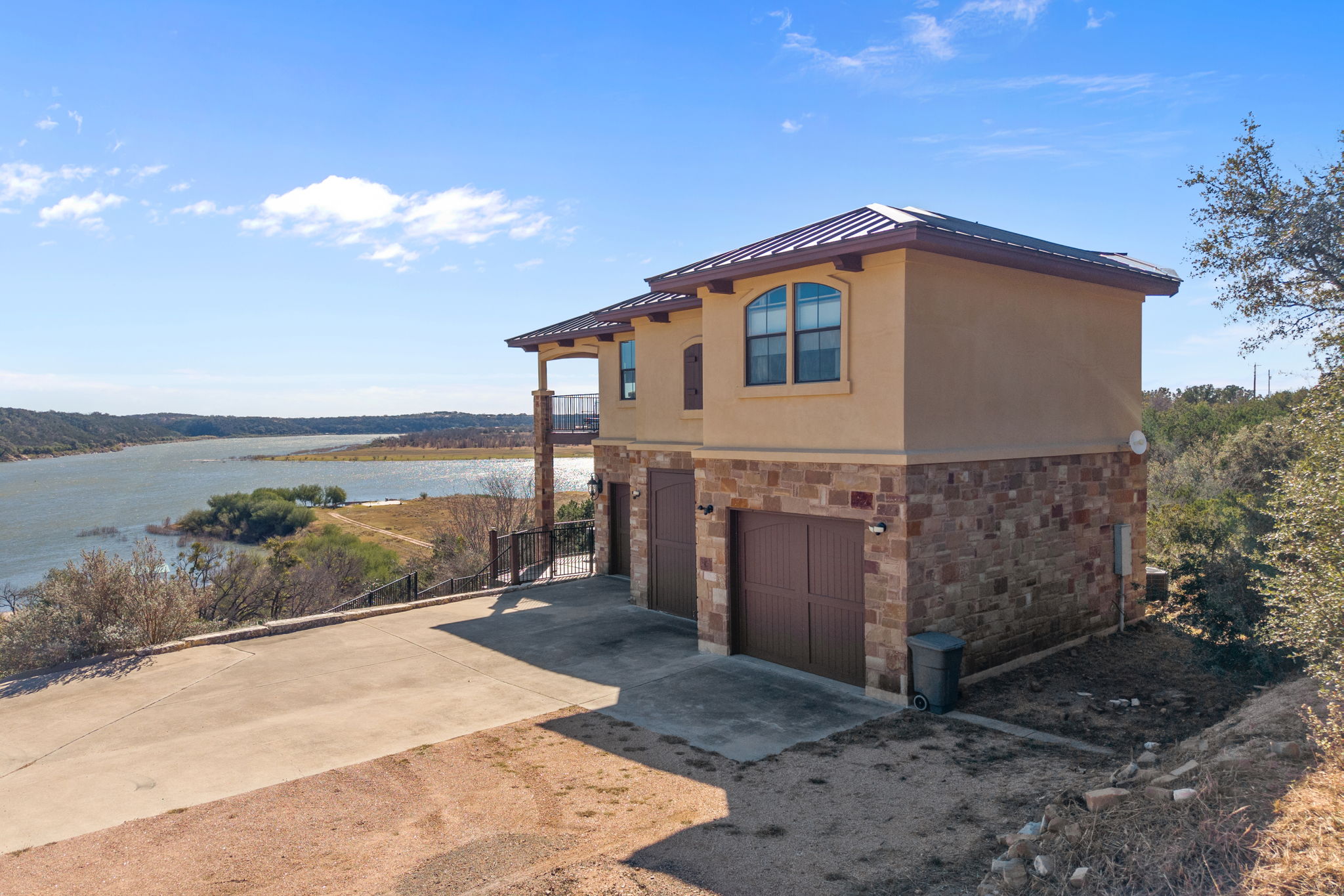 View of side of property featuring stone siding, a standing seam roof, stucco siding, an attached garage, and driveway