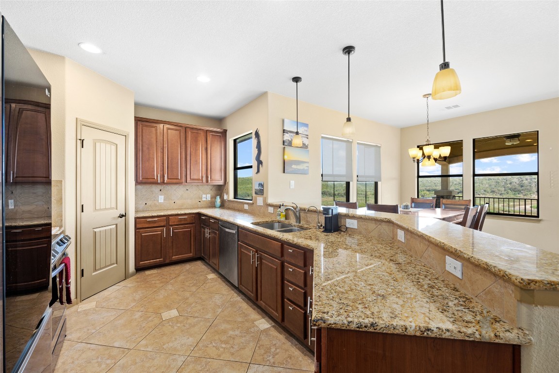 1690 Hickory Creek Road Marble Falls, TX 78654 - Photo 8 of 25 Kitchen with a chandelier, a peninsula, hanging light fixtures, decorative backsplash, and appliances with stainless steel finishes