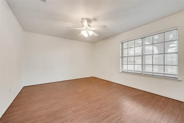 an empty room with wooden floor fan and windows