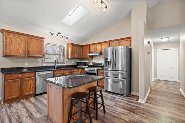 a kitchen with granite countertop stainless steel appliances a refrigerator a stove top oven and wooden floors