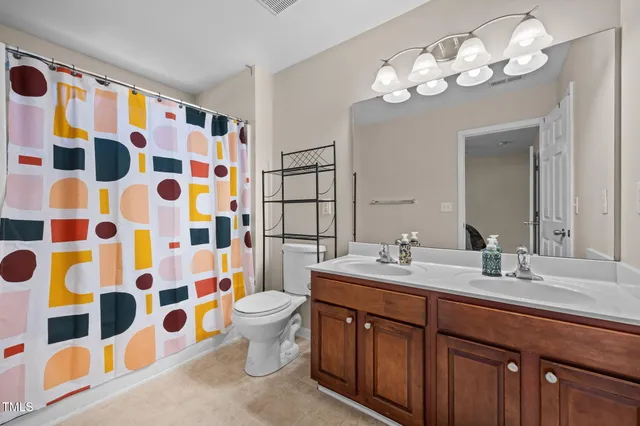 a bathroom with a sink a toilet a mirror a shower curtain and wooden floor