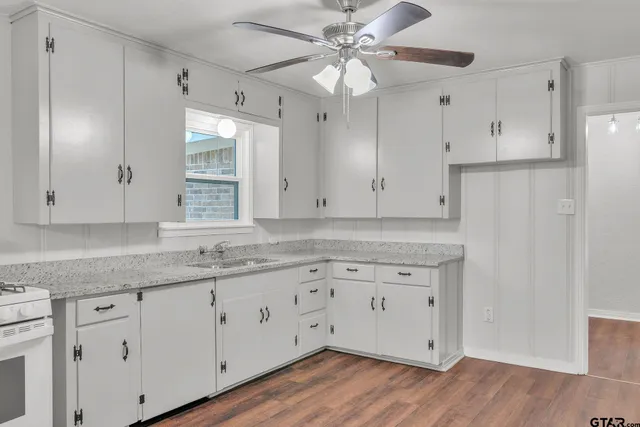 a kitchen with granite countertop white cabinets white appliances and a wide window
