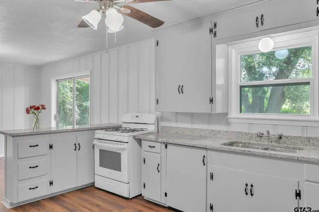 a kitchen with granite countertop white cabinets white appliances a large window and a sink