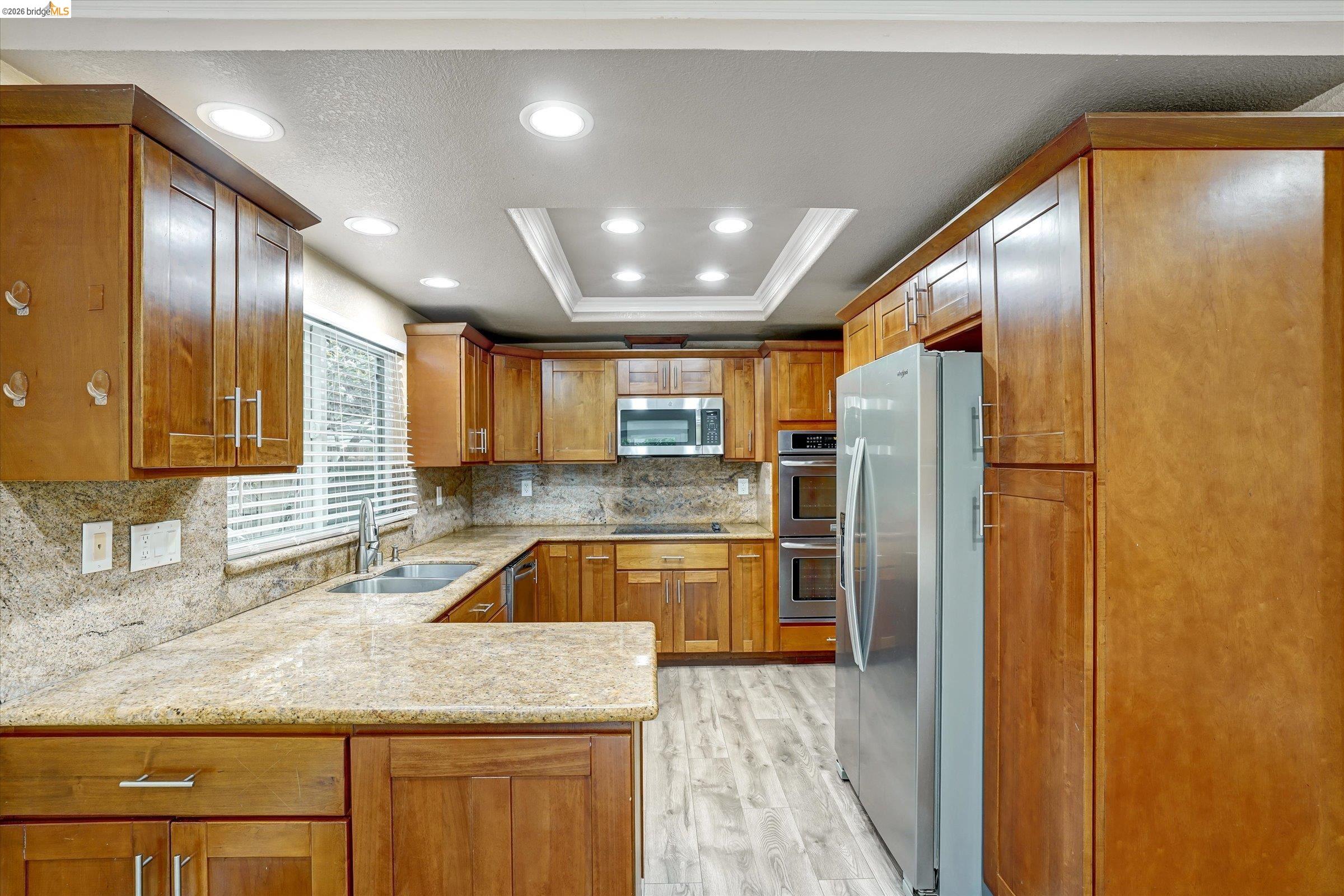 108 Castleton Court San Ramon, CA 94583 - Photo 14 of 41 Kitchen featuring stainless steel appliances, wood finish cabinets, light stone countertops, a peninsula, and light wood-style flooring