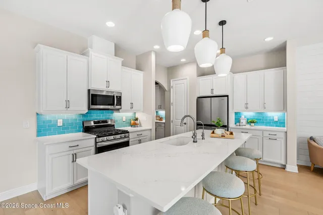 an open kitchen with a sink dishwasher white cabinets and couches with wooden floor