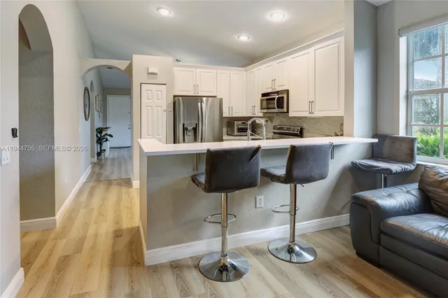 a living room with stainless steel appliances kitchen island granite countertop a table chairs refrigerator and sink