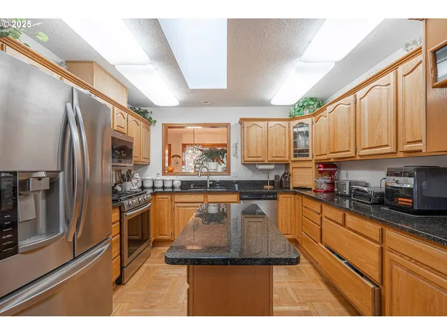 a kitchen with stainless steel appliances granite countertop a refrigerator a stove top oven and a sink with wooden floors