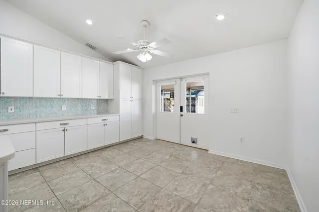 a view of an empty room with chandelier fan and kitchen view