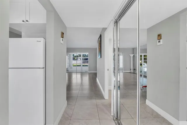 a view of a refrigerator in kitchen and an empty room with wooden floor