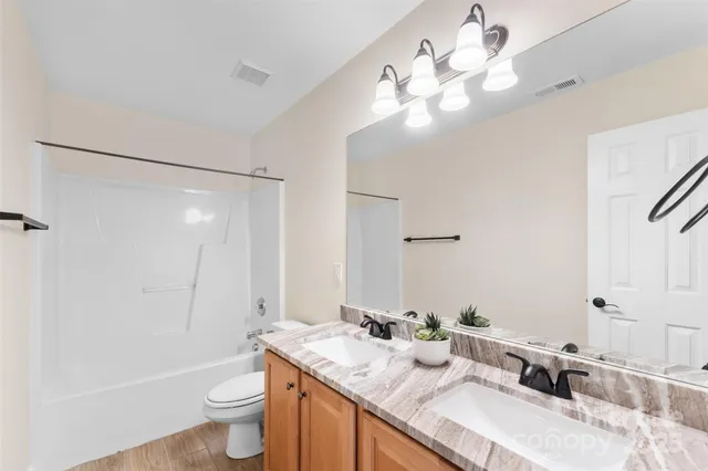 a bathroom with a granite countertop sink a toilet a mirror and shower