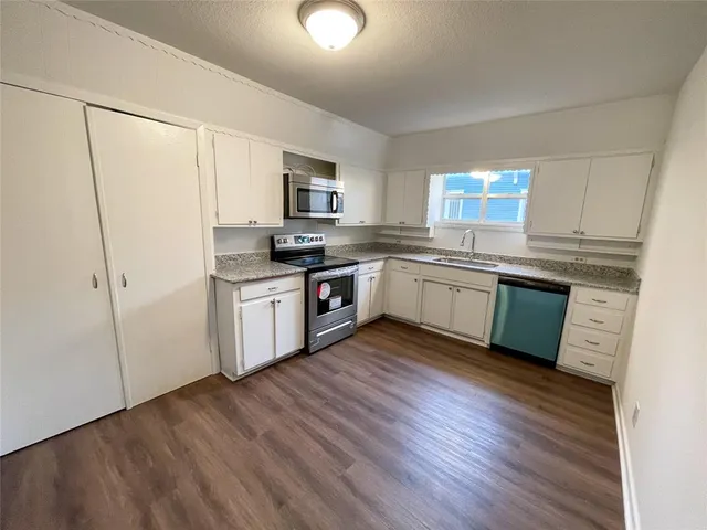 a kitchen with stainless steel appliances granite countertop a stove top oven a sink and white cabinets with wooden floor