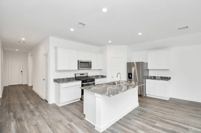 a kitchen with stainless steel appliances a stove top oven a sink a refrigerator white cabinets and wooden floor