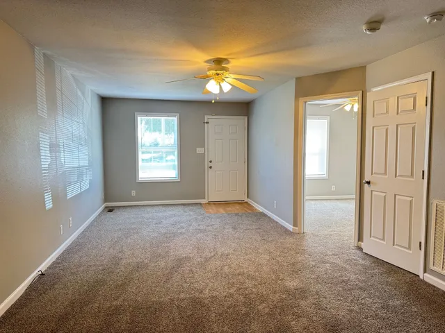 an empty room with windows and chandelier fan