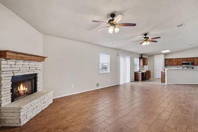 a view of a livingroom with a fireplace a ceiling fan and kitchen view
