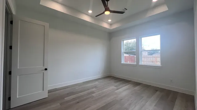 an empty room with wooden floor ceiling fan and windows