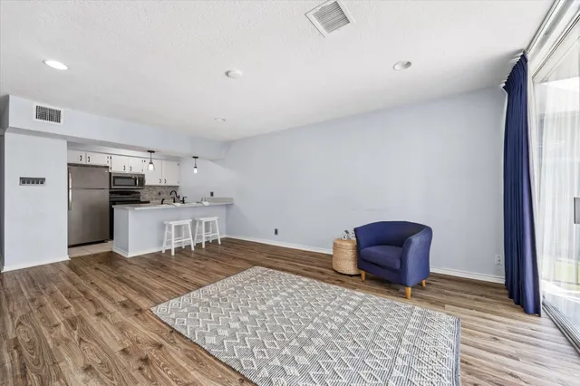 a living room with stainless steel appliances kitchen island granite countertop a refrigerator stove oven with white cabinets and wooden floor