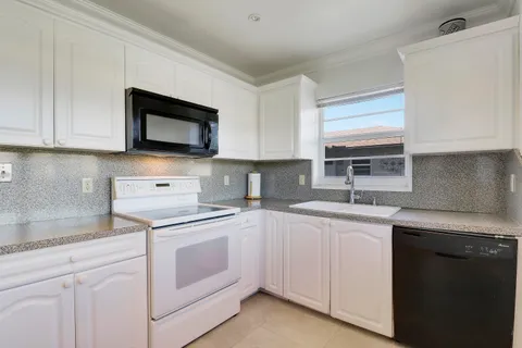 a kitchen with white cabinets appliances a sink and a window
