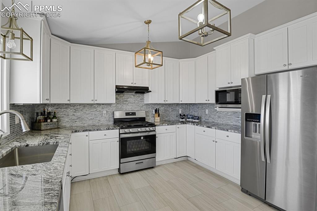 3805 Curtis Road Peyton, CO 80831 - Photo 9 of 36 a kitchen with granite countertop a refrigerator a stove a sink and white cabinets