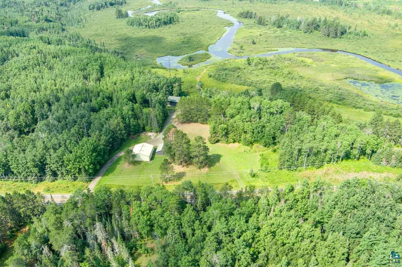 7603 Levander Road Embarrass, MN 55732 - Photo 51 of 51 Aerial view of a rural property featuring a residence nestled among mature coniferous and deciduous forest, with a natural waterway meandering through the landscape and cleared pastureland visible throughout the grounds