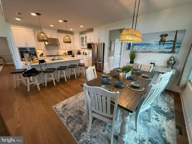 a kitchen with stainless steel appliances granite countertop a stove top oven a sink a dining table and chairs with wooden floor