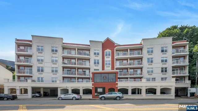a front view of a building with lot of cars and trees