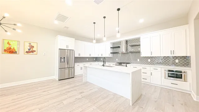 a kitchen with stainless steel appliances granite countertop a stove a sink dishwasher a refrigerator and white cabinets with wooden floor