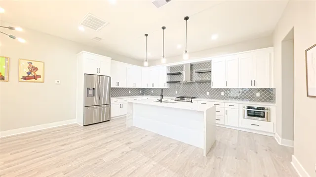 a kitchen with stainless steel appliances kitchen island granite countertop a refrigerator a sink dishwasher a stove and white cabinets with wooden floor