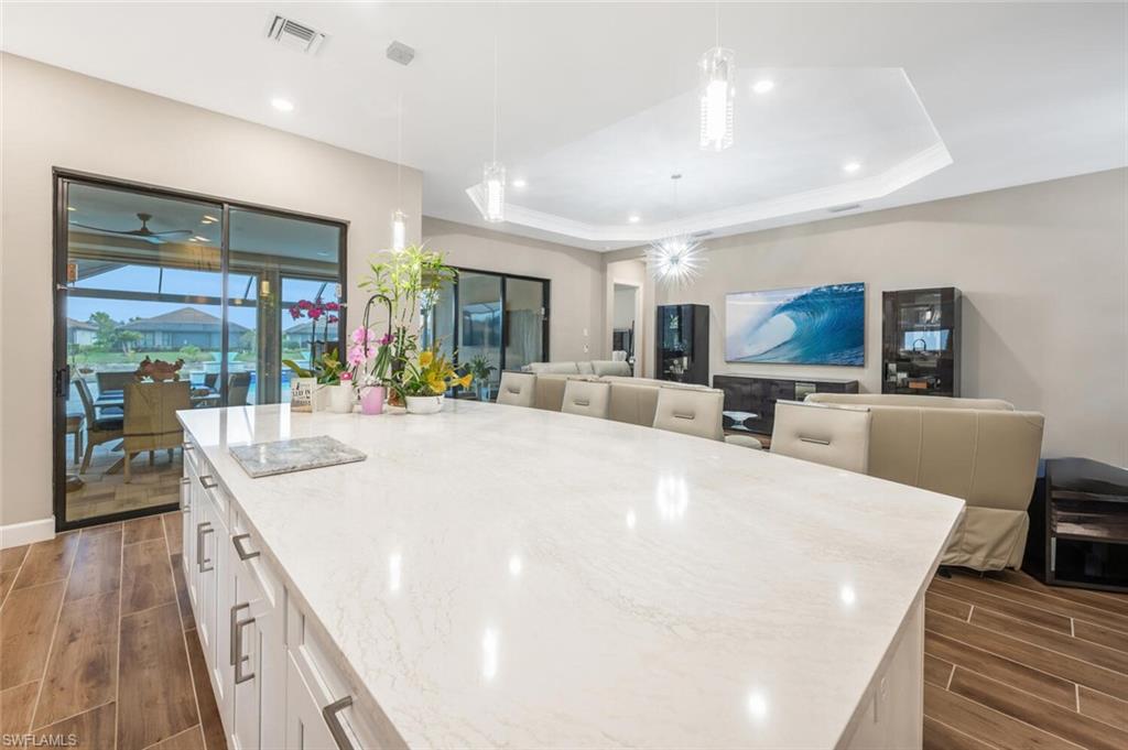 8416 Rosa Court Naples, FL 34114 - Photo 10 of 34 Spacious open-concept living area featuring an expansive kitchen island with a light-toned countertop, white cabinetry with contemporary pulls, wood-finish flooring, and a tray ceiling