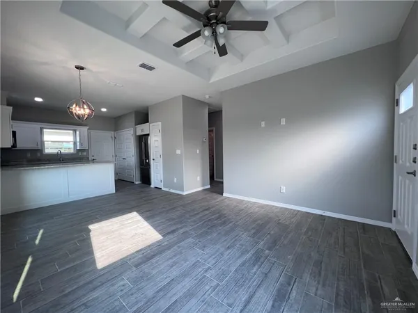 an empty room with wooden floor and kitchen view