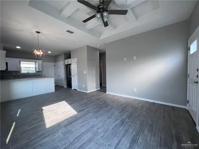 an empty room with wooden floor and kitchen view