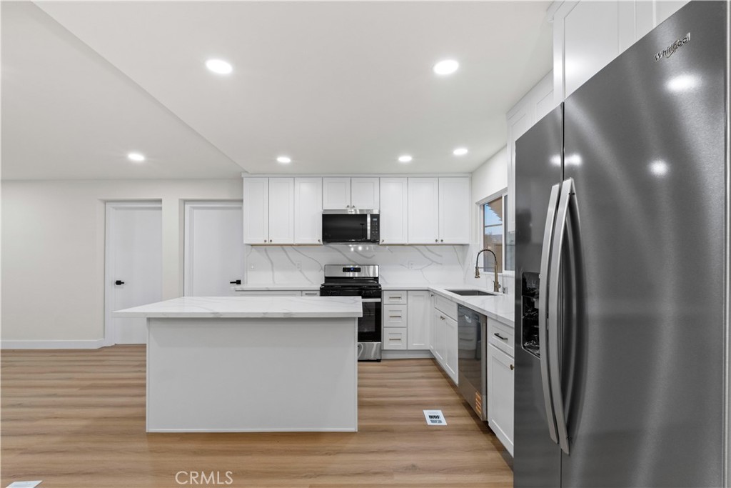 33195 Meyer Road Nuevo, CA 92567 - Photo 10 of 36 a large kitchen with stainless steel appliances kitchen island a sink dishwasher a refrigerator and white cabinets with wooden floor