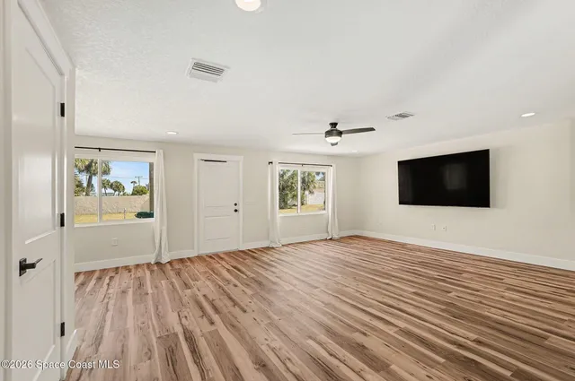 a view of empty room with wooden floor and fan